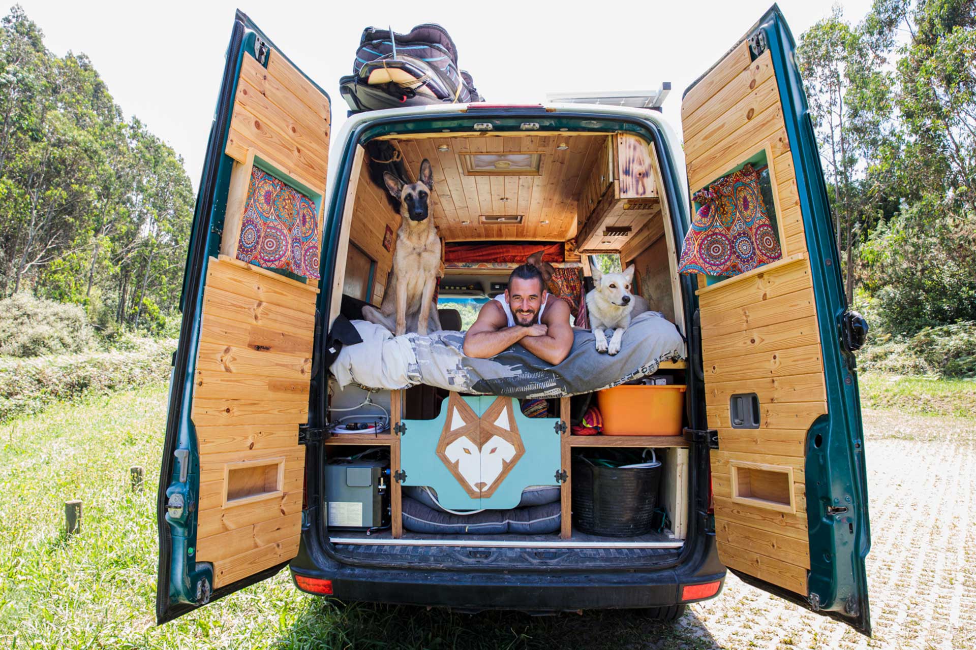 Selbst ausgebautes Wohnmobil mit maßgefertigtem Holzausbau, zwei Hunden und einem entspannten Besitzer, der die Flexibilität des DIY-Campers genießt.